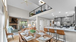 Un comedor amplio con una mesa de madera dispuesta para seis comensales, una cocina con electrodomésticos modernos y un balcón con vistas.
