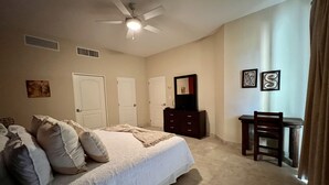 A bedroom with a bed, dresser, chair, ceiling fan, and artwork on the wall. - Beguiling pool-ocean view unit (La Paz)
