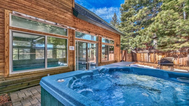 Een houten vakantiehuis met grote ramen, een jacuzzi en een omheinde achtertuin met bomen.