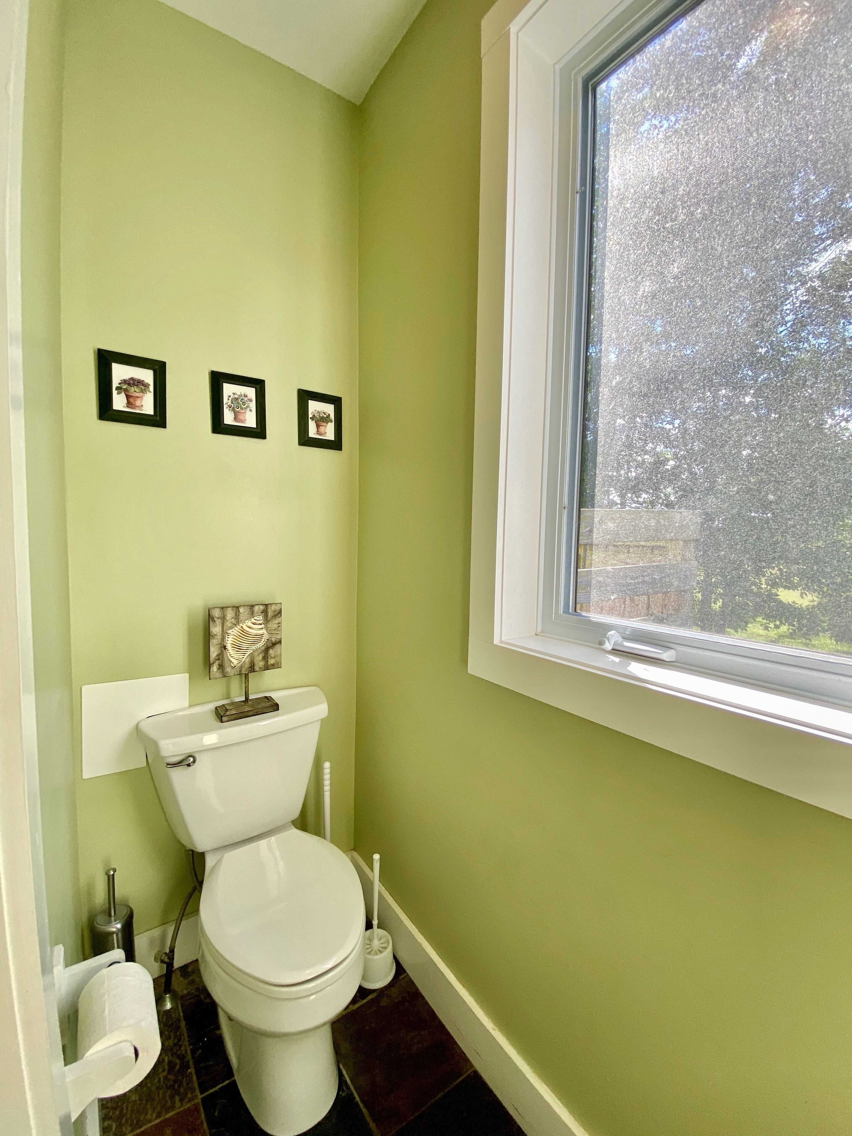 A bathroom with a toilet, a window, and three framed pictures on the wall.