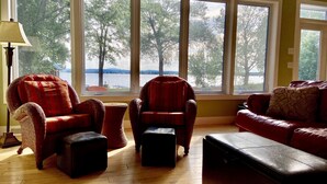 Un salon avec une grande fenêtre, des fauteuils en osier, un canapé en cuir et une lampe.