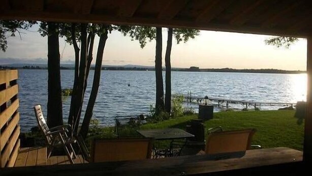 Un espace extérieur aménagé avec des sièges, offrant une vue sur un lac, entouré d’arbres et doté d’une terrasse en bois.