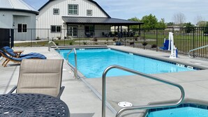 Une piscine entourée d’une clôture, avec des chaises longues et une table, et une maison en arrière-plan.