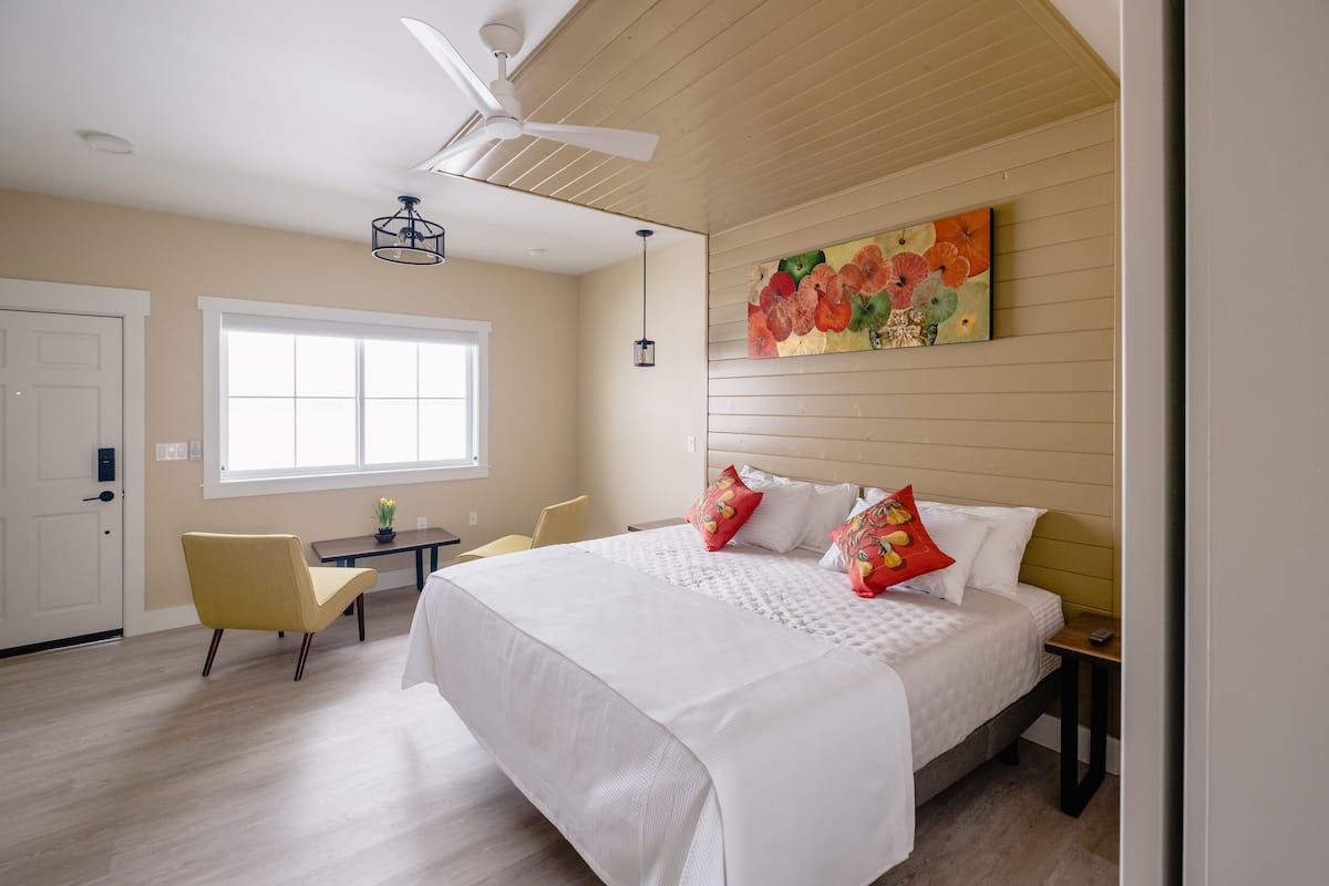Un dormitorio con una cama grande, un ventilador de techo, una ventana, un escritorio y una silla.