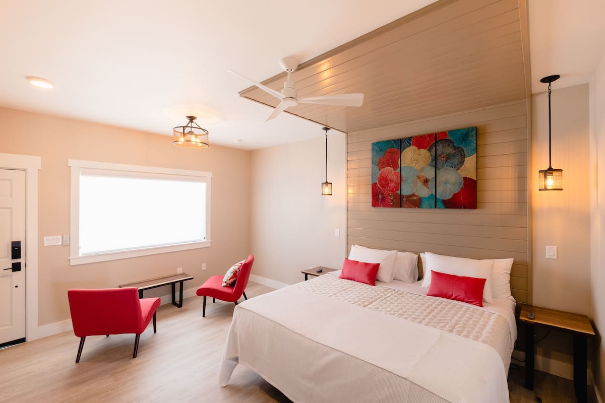 Un dormitorio con una cama, una silla roja, un escritorio y un ventilador de techo.