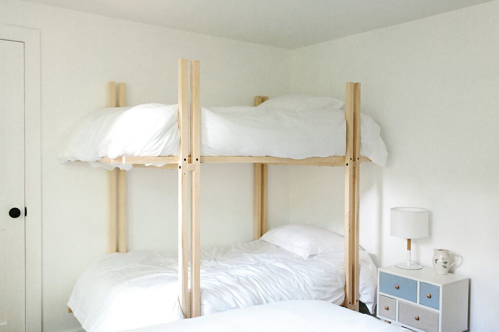 A bunk bed with white bedding and a bedside table with a lamp and a pitcher.