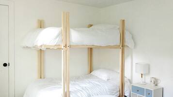 A bunk bed with white bedding and a bedside table with a lamp and a pitcher.