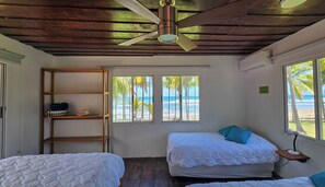 A room with two beds, a ceiling fan, a wooden shelf, and a window with a view of the beach. - Air conditioner in all the bedrooms, swimming pool, experience the pura vida!  (Guanacaste)