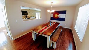 Comedor con una mesa de madera y bancos, una araña y la bandera del estado de Colorado en la pared.