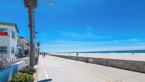 A coastal walkway with a clear sky, palm trees, and a beach in the background. - Newly Remodeled! Oceanfront Mission Beach Condo Sleeps 6 with Incredible Views! (San Diego)