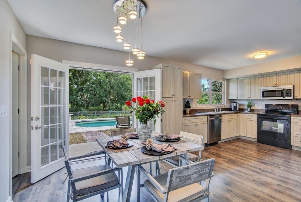 A modern kitchen with an open layout, a dining area with a table set for two, and a view of a swimming pool.