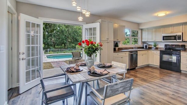Una cucina moderna con disposizione aperta, un'area pranzo con tavolo imbandito per due e vista su una piscina.