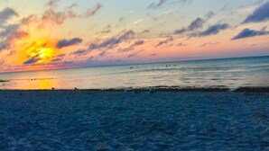 Een strand met een zonsondergang, een rustige zee en mensen in de verte.
