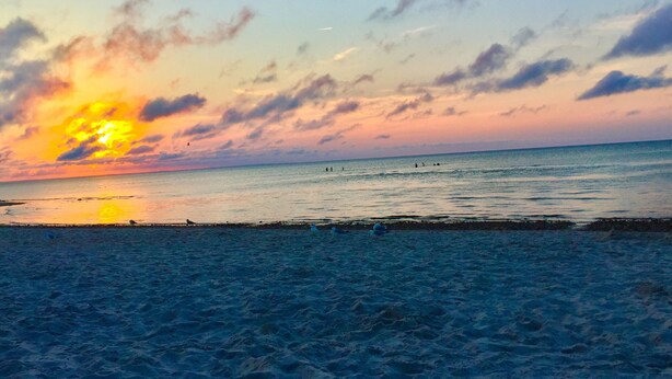 Ein Strand bei Sonnenuntergang, ruhiges Meer und Personen in der Ferne.