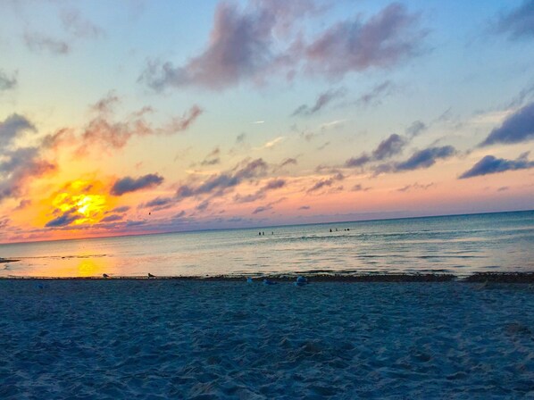 Una spiaggia al tramonto, con mare calmo e persone in lontananza.