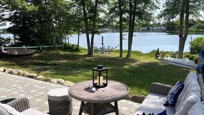 Een terras met rieten meubels, een ronde tafel met kaarsen, en uitzicht op een meer.