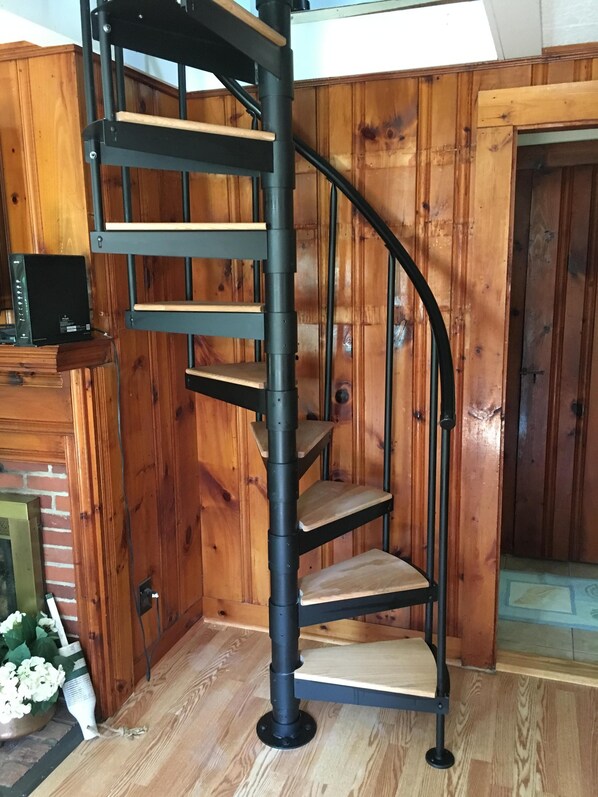 Eine Wendeltreppe mit Holzbodenstufen und schwarzen Metallgeländern in einem Raum mit Holzwänden und einem Kamin aus Ziegelsteinen.