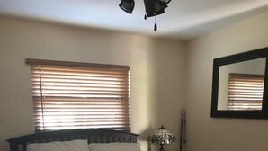 A bedroom with a wooden bed, white pillows, a quilt, a nightstand, a lamp, and a mirror.