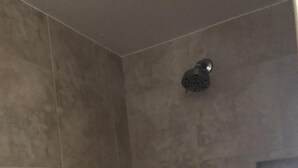 A bathroom with a shower, a small shelf, and a mirror.