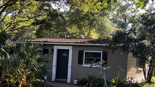 A small, single-story house with a dark brown exterior, white trim, and a tiled roof.