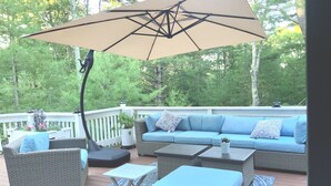 A deck with wicker furniture, a large umbrella, and a view of trees.