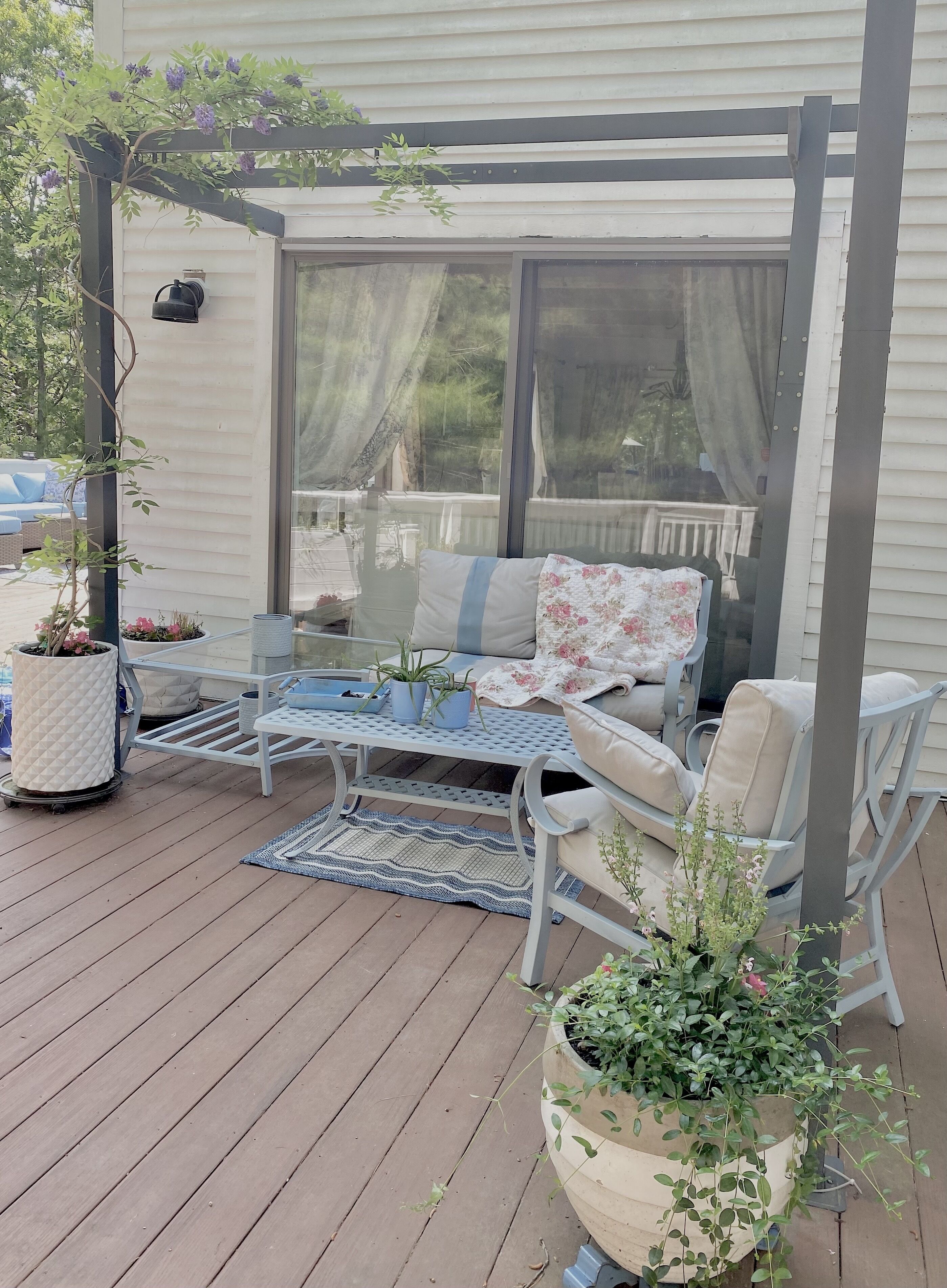 Een overdekt terras met een bank, stoelen, een tafel en potplanten.
