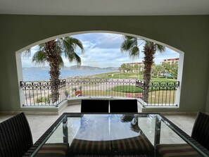 A balcony with a glass table and chairs, overlooking a beach and a resort area. - Charming sunset ocean view unit (La Paz)