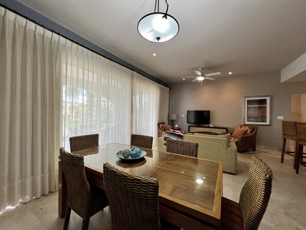 A spacious living room with a large dining table surrounded by wicker chairs, a sofa, and a television. - Charming sunset ocean view unit (La Paz)