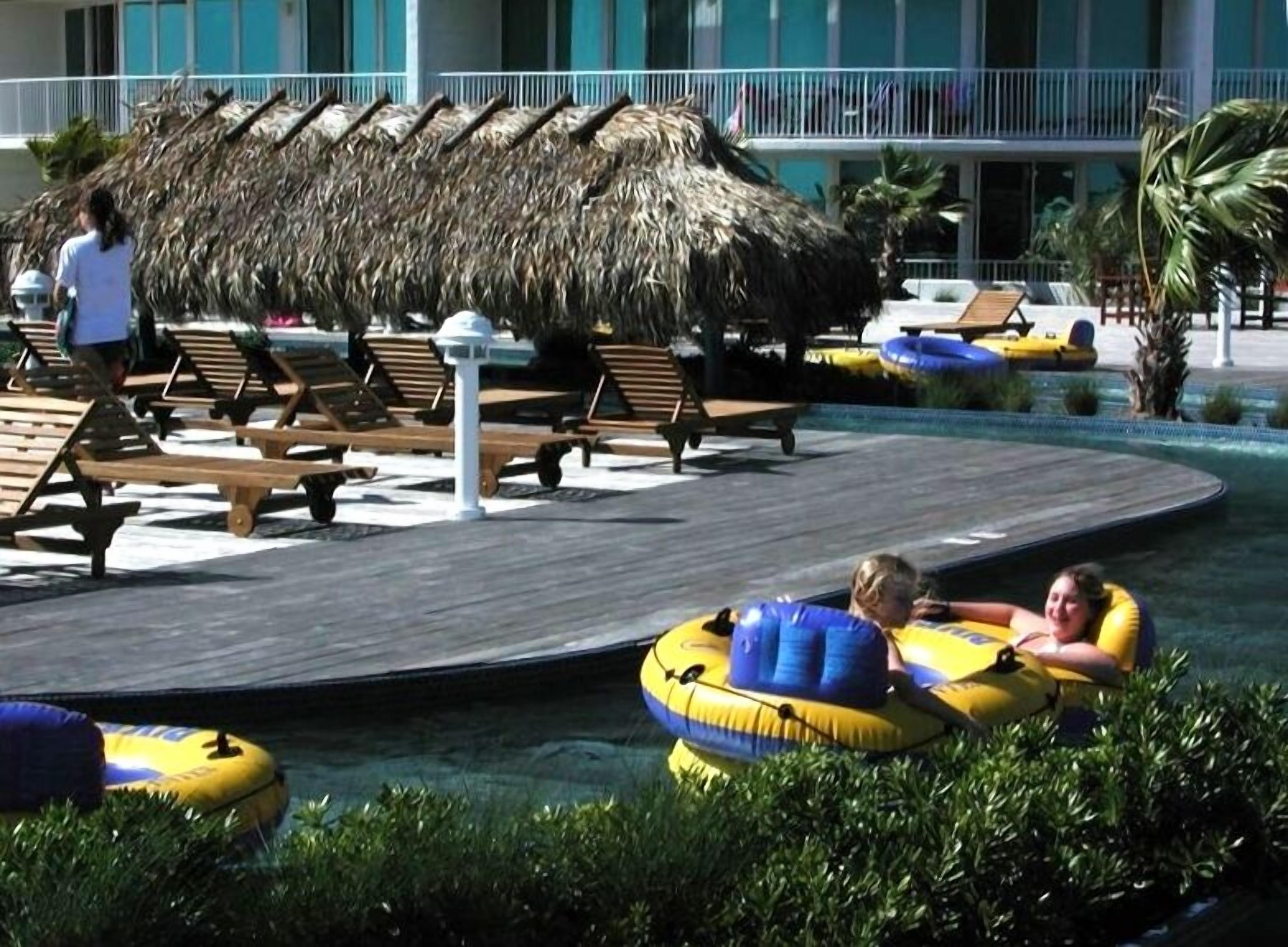 A pool area with lounge chairs and a thatched structure.