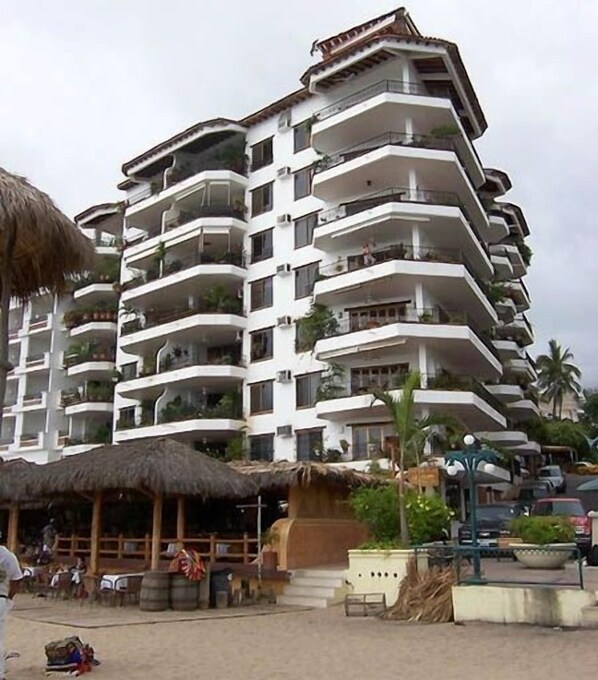 Un hotel de varios pisos con balcones, una estructura de techo de paja y un área pavimentada con asientos.