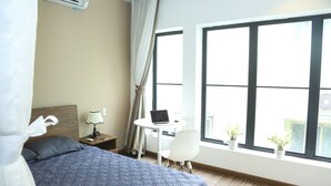 A hotel room with a bed, a desk with a laptop, a chair, and a window with potted plants. - Min Apartment (Ho Chi Minh City)
