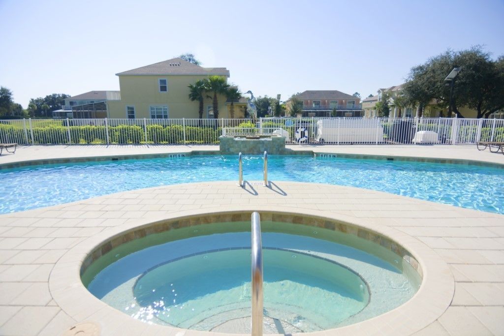A swimming pool with a hot tub in the center, surrounded by a white fence and a paved deck.