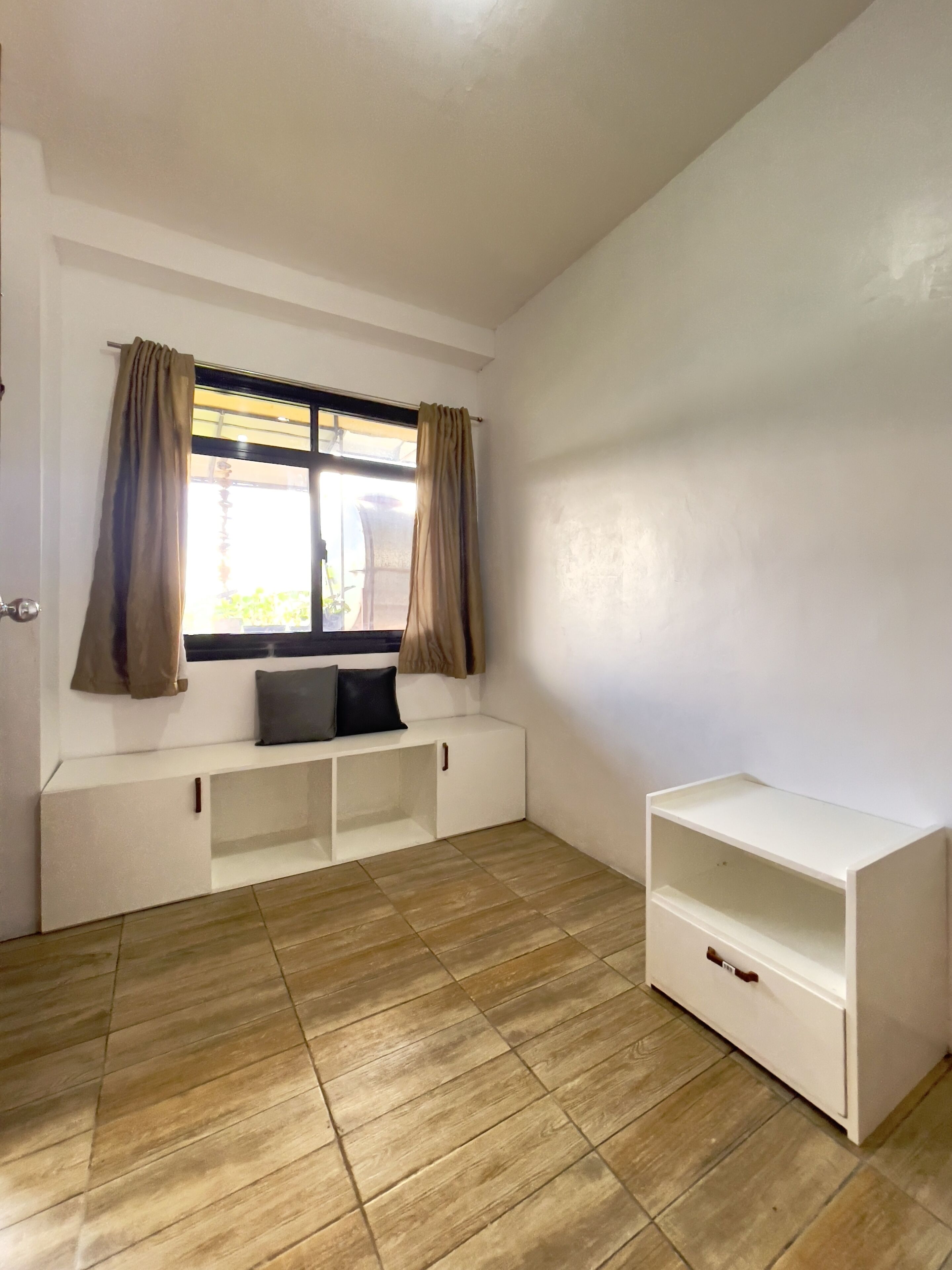 A room with a window, a bench, and a white cabinet.