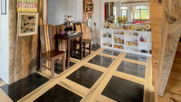 Un intérieur rustique avec des poutres en bois, un coin repas avec une table et des chaises en bois, et une étagère blanche où sont disposés divers objets.