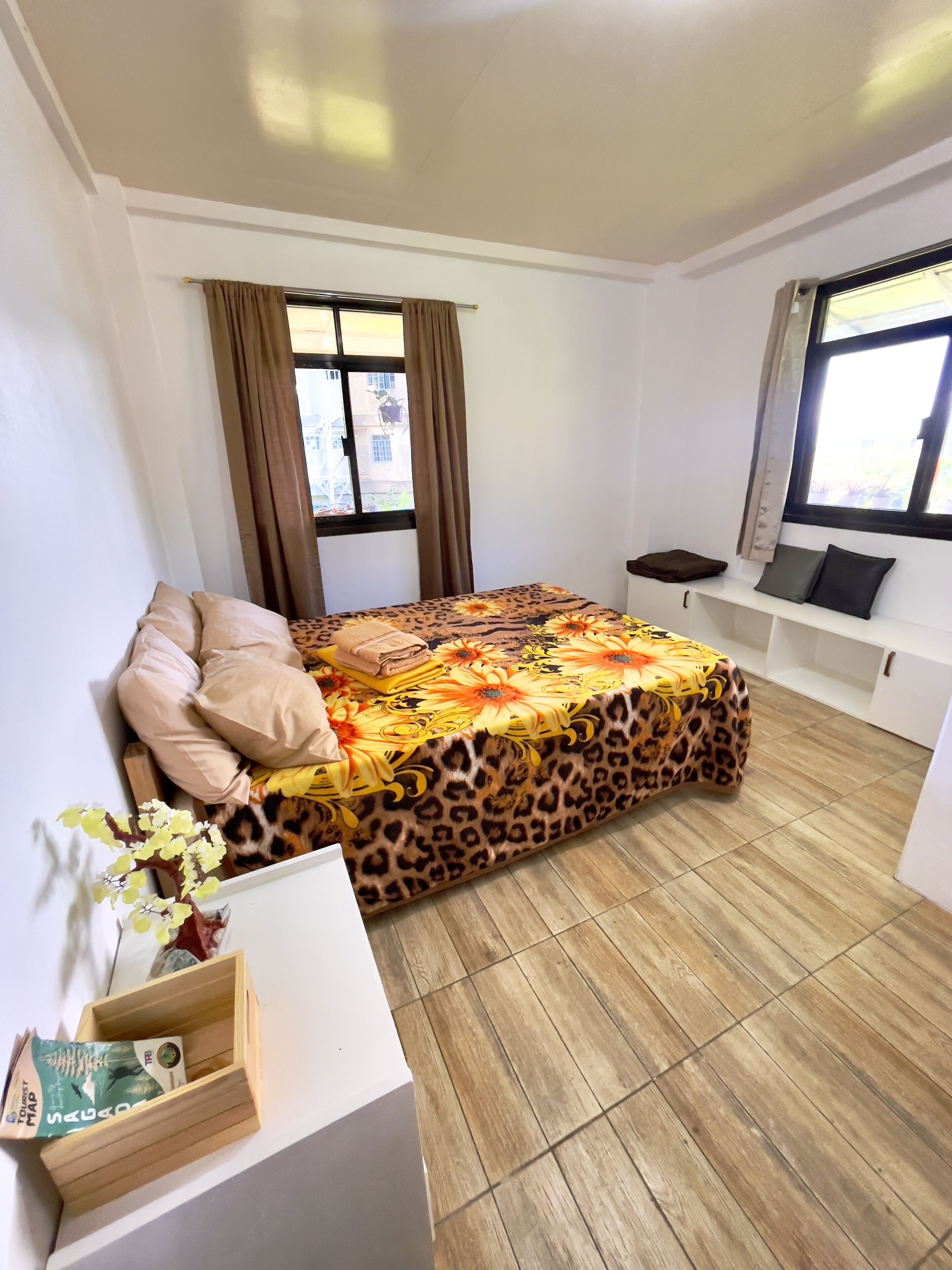 A bedroom with a bed, a bedside table, a window, curtains, and a view of the outside.