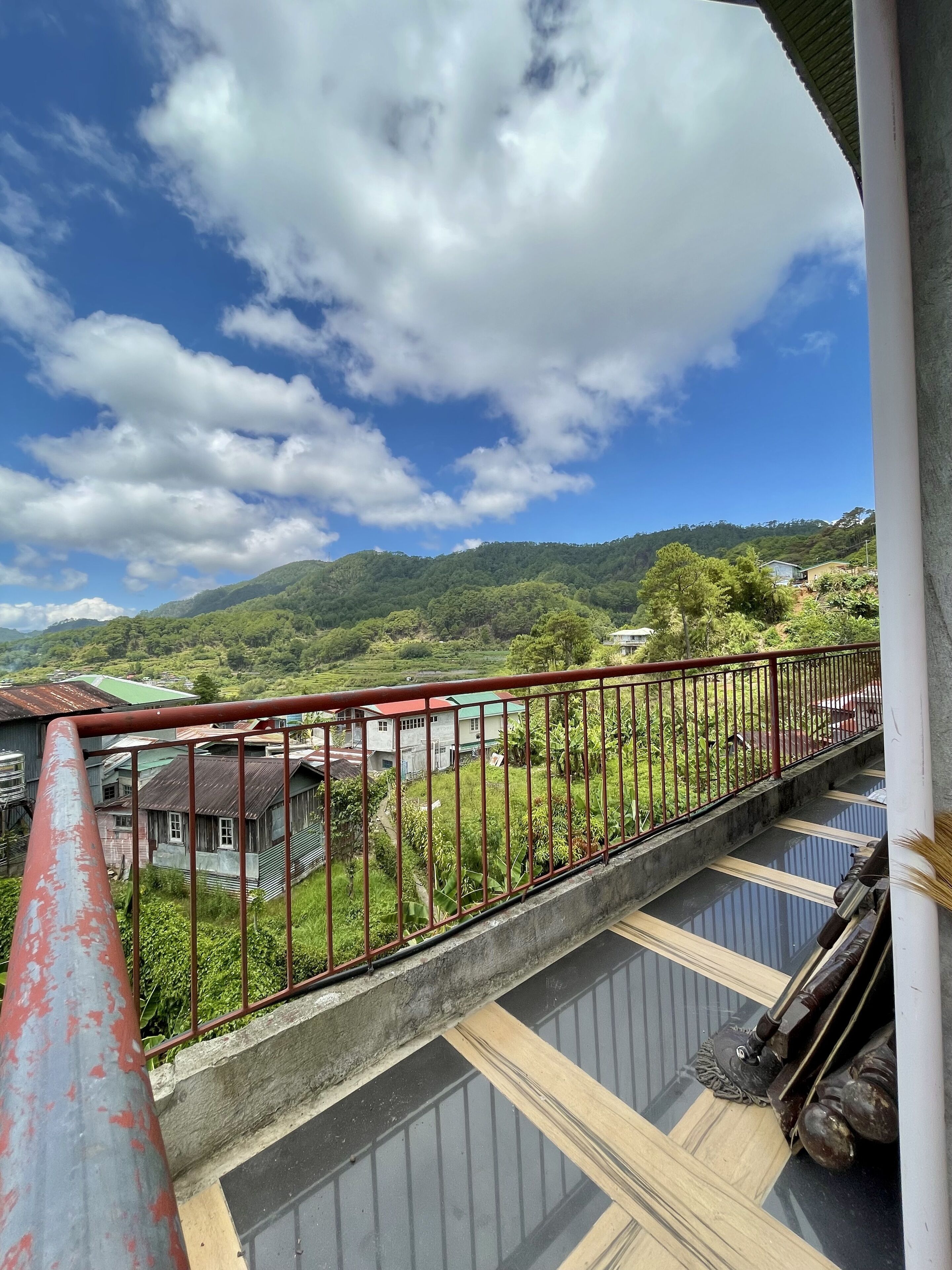Varanda com guarda-corpo vermelho com vista para uma paisagem verde exuberante e céu azul límpido.