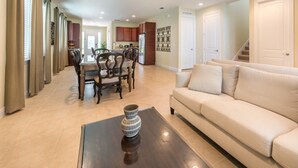 A spacious living room with a beige sofa, a dining area with a wooden table and chairs, and a kitchen in the background. - Aco255240 - The Encore Club Resort - 8 Bed 7 Baths Villa (Kissimmee)