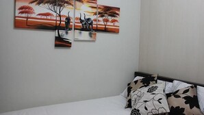 Ein Schlafzimmer mit einem Bett, einem Nachttisch und drei Bildern, die eine Savannenszene mit Elefanten und Bäumen zeigen.