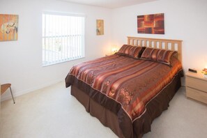 Un dormitorio con una cama grande, una ventana con persianas, una mesita de noche y una mesilla.