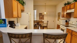 A kitchen with wooden cabinets, a white countertop, two wicker chairs, a dining area with a table and chairs, and a hanging light fixture. - Ahr105 - Sunset Ridge - 5 Bed 3 Baths Villa (Davenport)