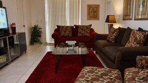 A living room with a red rug, a glass coffee table, a red sofa, a brown sofa, and patterned cushions. - Ahr105 - Sunset Ridge - 5 Bed 3 Baths Villa (Davenport)