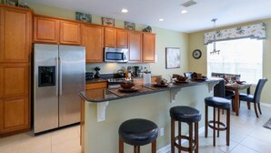 A kitchen with wooden cabinets, a stainless steel refrigerator, a microwave, and a dining area with a table and chairs. - Fv64670 - Windsor Hills Resort - 4 Bed 4 Baths Villa (Kissimmee)