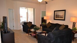A living room with a dark-colored sofa set, a coffee table, a TV stand, and a framed picture on the wall. - Ip60393 - The Shire at West Haven - 4 Bed 3 Baths Villa (Davenport)