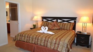 A neatly made bed with a brown and beige striped bedspread, two pillows, and a swan-shaped towel arrangement. There are two bedside tables with lamps, and a door leading to another room. - Ip60393 - The Shire at West Haven - 4 Bed 3 Baths Villa (Davenport)