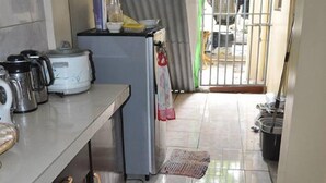 A compact kitchen with a refrigerator, a stove, and various appliances on the counter. - Haus Of Tubo Pension House (Davao)