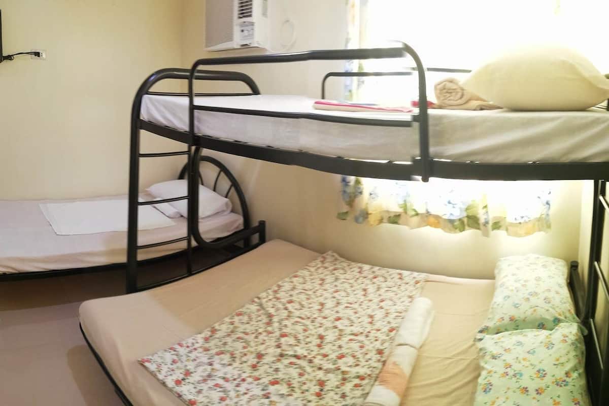 A bunk bed room with a television mounted on the wall, an air conditioner, and a window with curtains.
