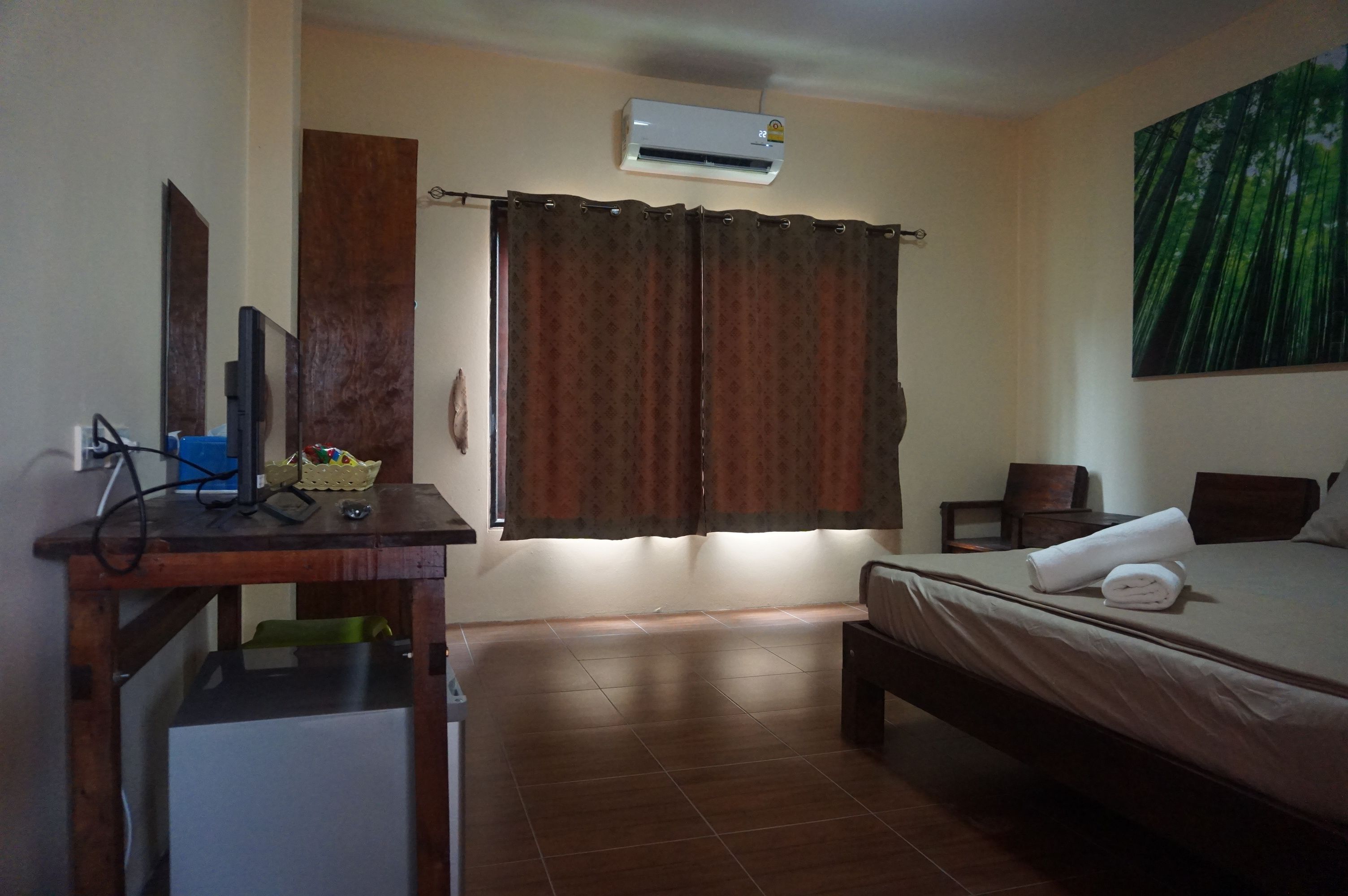 A hotel room with a bed, a desk with a computer, an air conditioner, and a painting on the wall.