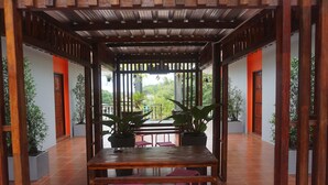 A covered outdoor seating area with a wooden table and chairs, surrounded by potted plants and a view of greenery. - Thai House Hotel & Resort Hat Yai (Hat Yai)