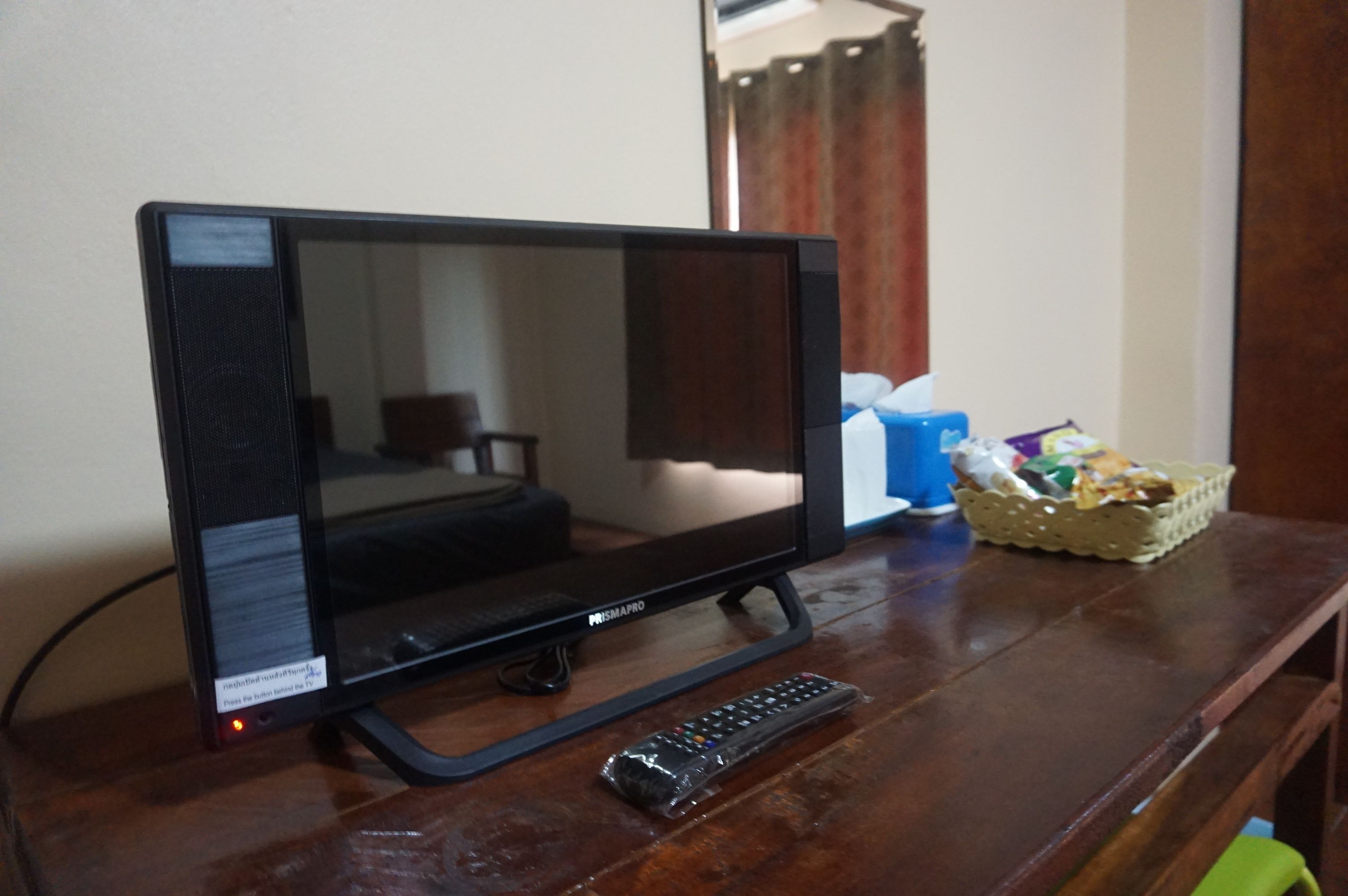 Televisor de pantalla plana sobre una superfície de fusta, amb un comandament a distància i un cistell de llaminatures.