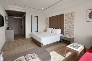 Una habitación de hotel moderna con una cama grande, mesitas de noche, una pequeña mesa de lectura y un sofá rojo.